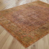 An antique-style distressed area rug with a complex multicolor pattern in shades of mink and soft olive green, shown laid out on a light-colored wooden plank floor.