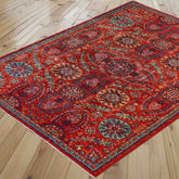A traditional area rug with a vibrant red base and intricate multicolour floral patterns, shown laid out on a light wood plank floor.