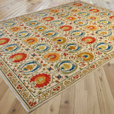 A rectangular area rug with an ornate traditional floral and medallion pattern in cream, blue, red, yellow, and green, shown laid out on a light wood plank floor.