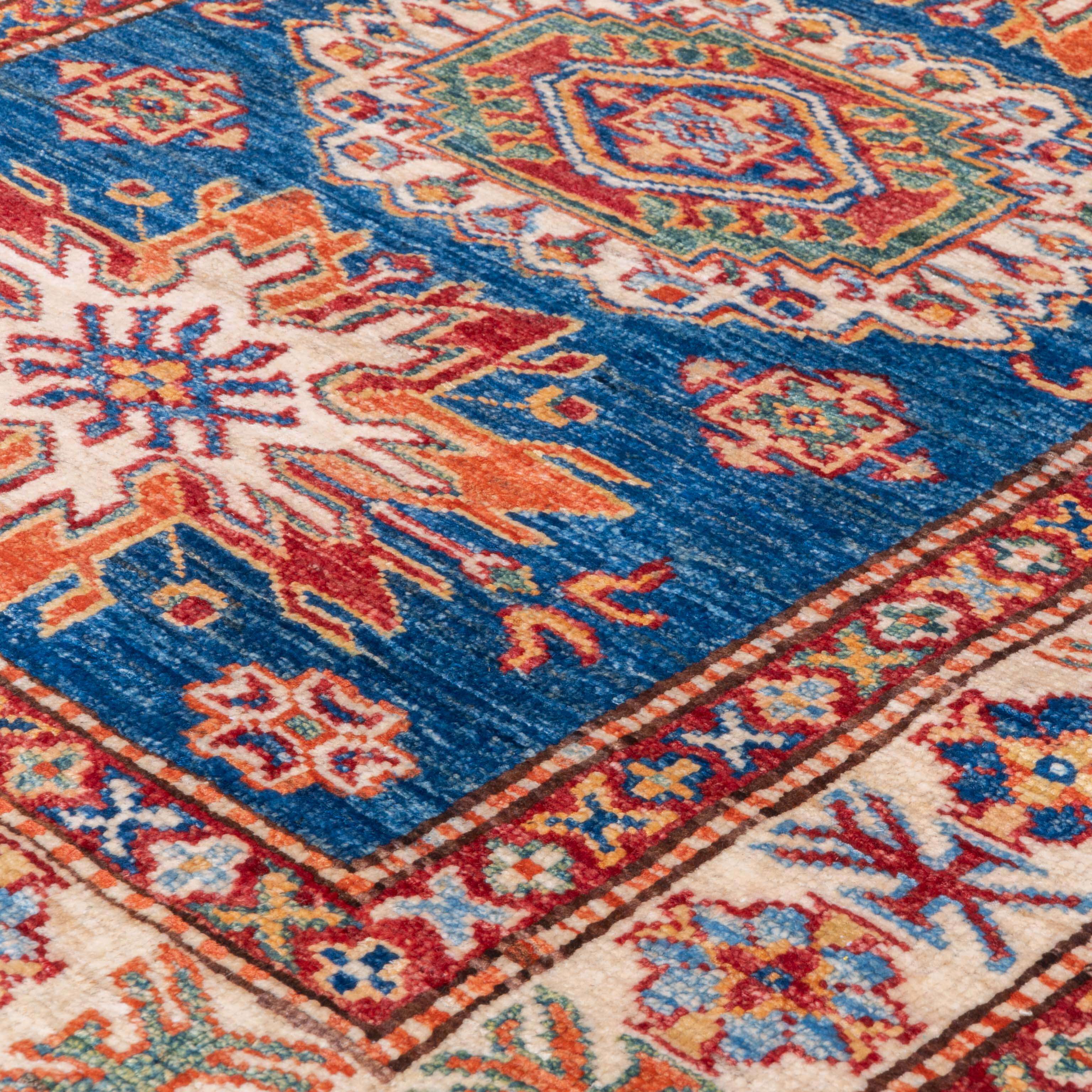 A close-up of a traditional patterned area rug with a deep blue field, cream borders, and red, orange, and green ornamental motifs.