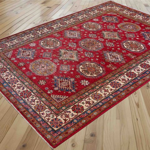 A traditional Persian-style area rug with a vibrant red field and intricate geometric medallions, displayed on a light-colored wooden floor.