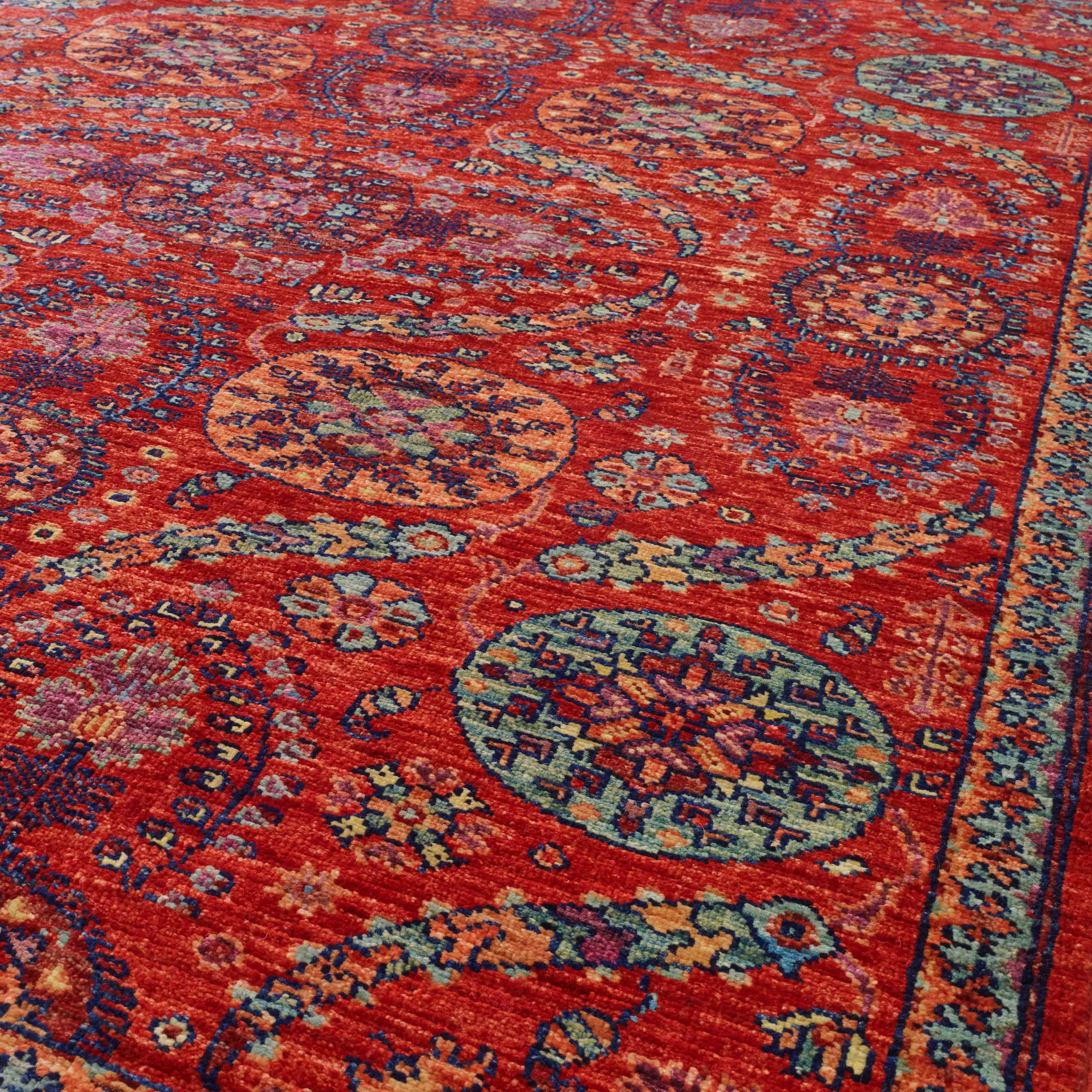 A close-up view of a traditional patterned area rug with a vibrant red base and intricate medallion motifs in peach, green and heather.