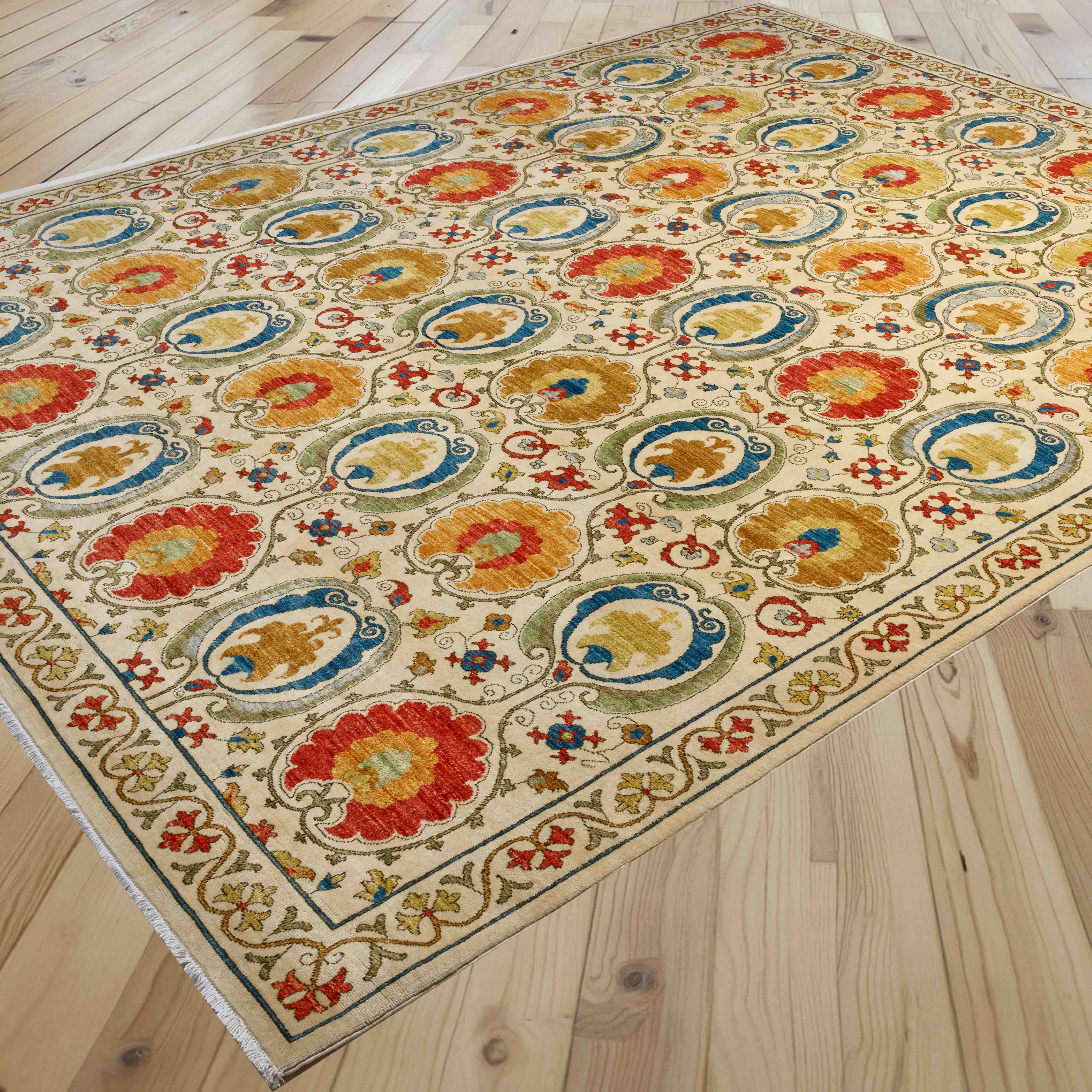 A rectangular area rug with an ornate traditional floral and medallion pattern in cream, blue, red, yellow, and green, shown laid out on a light wood plank floor.