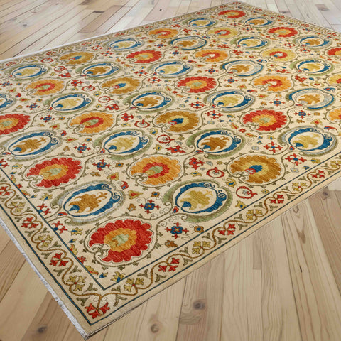 A rectangular area rug with an ornate traditional floral and medallion pattern in cream, blue, red, yellow, and green, shown laid out on a light wood plank floor.