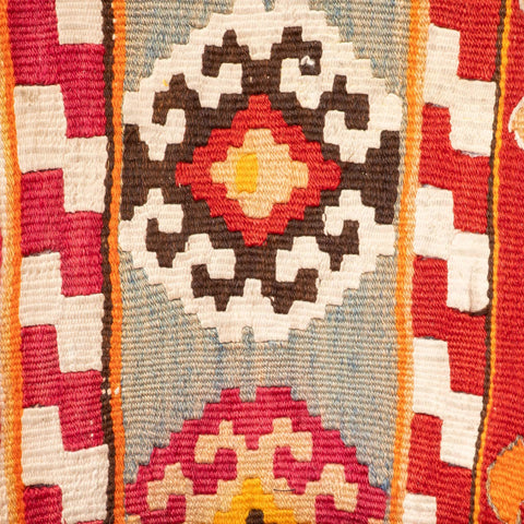 Close-up of a woven textile pattern with geometric motifs in red, cream, brown, orange, and light blue.