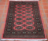 Rose red ground, with 14 motifs symmetrically laid out across the central section.  A broad border of decoration incorporating pattern work and smaller motifs.  All of the decorative work is in black with highlights in cream, peach and soft green. 