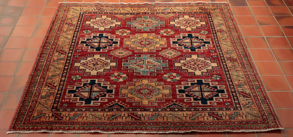 A beautiful hand made Afghan Kazak with a golden glow. The background colour is a soft tomato red with a gold border and cream and blues of different shades in the geometric diamond motifs. It is made from vegetable dyed Afghan wool from the Karakul sheep that roam the mountainous terrain in Afghanistan.