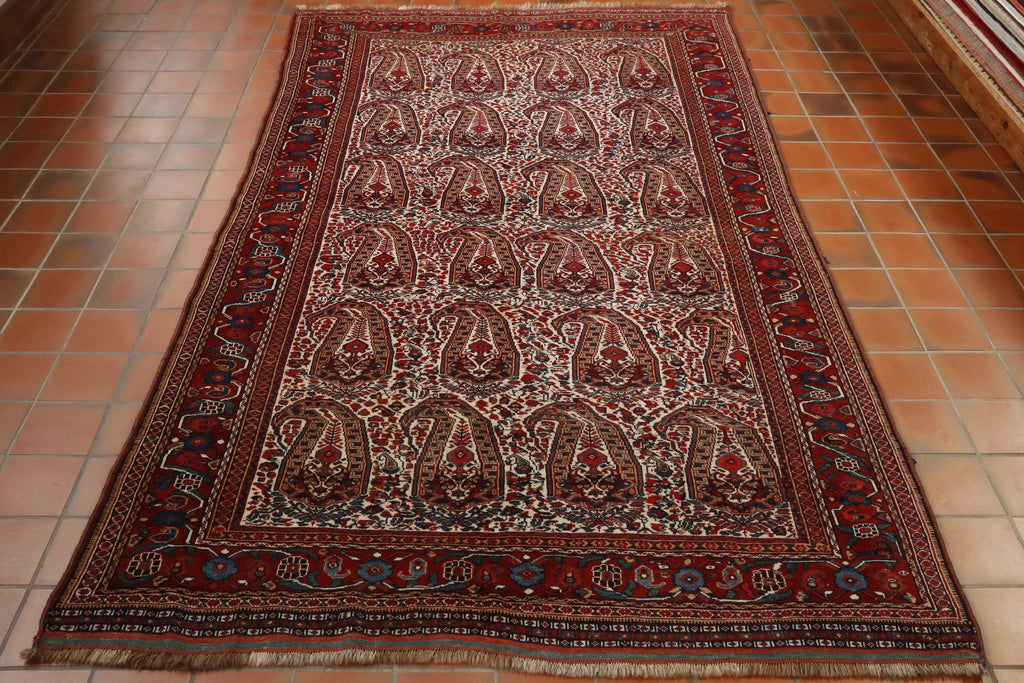 A series of mir boteh (paisly shapes) across the central ground.  The colours used in these are deep red, golden yellow dark blue on a cream ground.  With a border with a floral design on the deep red back ground.  