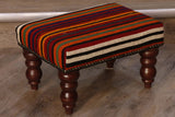 kilim covered stool covered in stripes of wine red, bright orange, black, gold and green