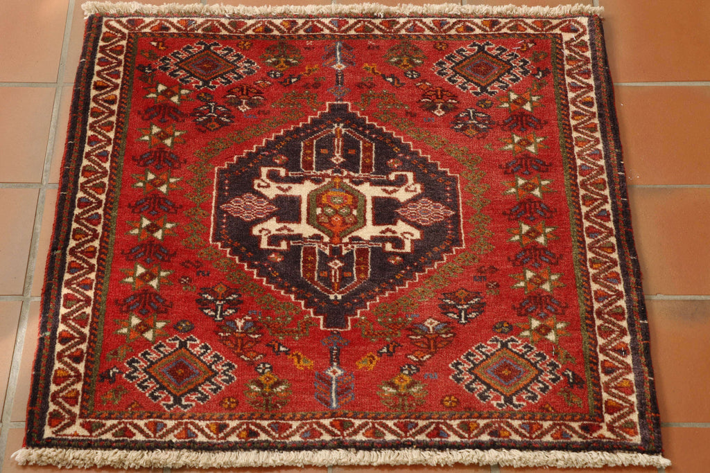 A lovely little tribal mat 60 by 60 centimetres.  Showcasing the traditional colours and designs used in the Qashqai rugs being a red ground with decoration in dark blue, olive green, orange and cream highlights.  The decoration shows various stylised flowers around a large central medallion.  