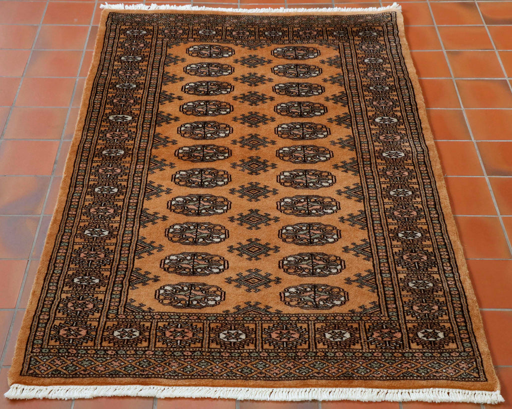 Pakistan Bokhara rugs have a lovely soft silky pile and a luxurios feel. Sometimes they are mistaken for silk but it is a fine wool knotted on to a cotton warp and weft. The main colour of this piece is an old gold. The design in the centre is a traditional repeating small lozenge in two vertical columns. Other colours used in the rug are peach, cream and very pale green.