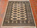 Pakistan Bokhara rugs have a lovely soft silky pile and a luxurios feel. Sometimes they are mistaken for silk but it is a fine wool knotted on to a cotton warp and weft. The main colour of this piece is beige. The design in the centre is a traditional repeating small lozenge in two vertical columns. Other colours used in the rug are peach, cream and pale grey.
