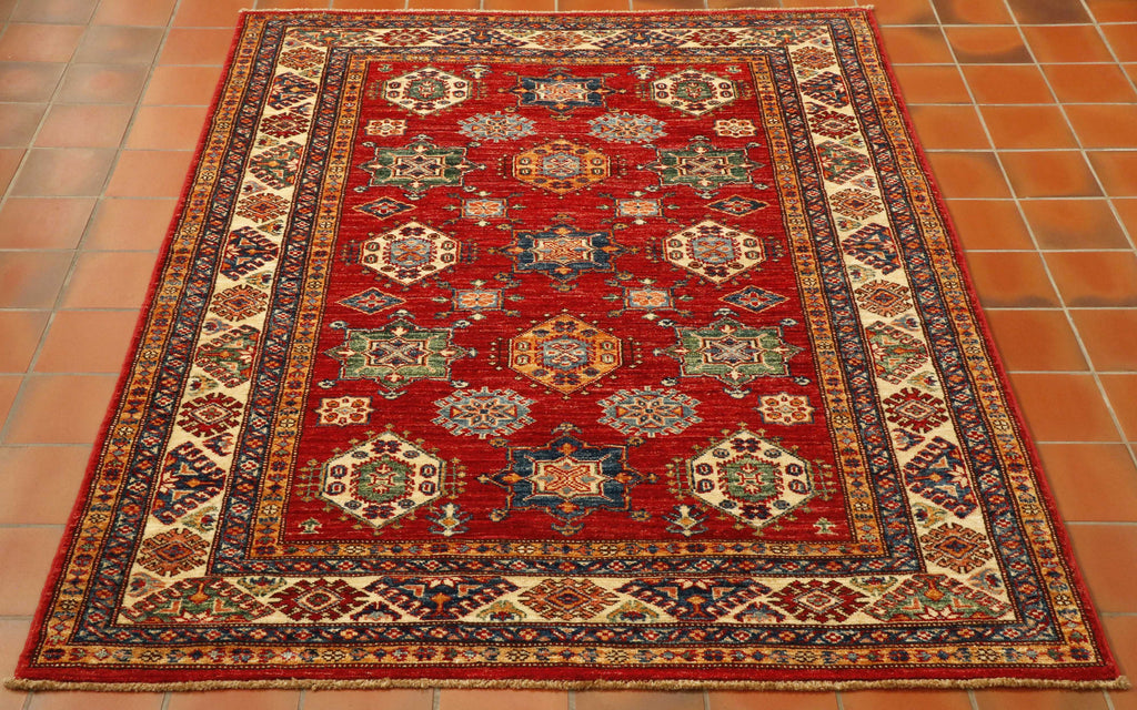 Bright red central ground, geometric medallions symmetrically laid out lupon it using a colour palette of cream, blue, green and golden yellow.  5 borders of varying sizes and designs but using the same colour palette, 